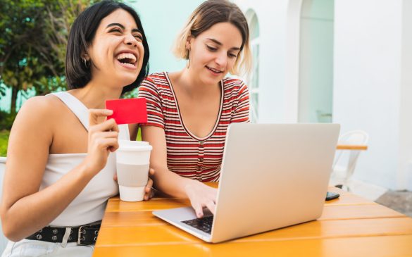 Portrait of two young friends doing online shopping with laptop and credit card at coffee shop. Shop online concept.